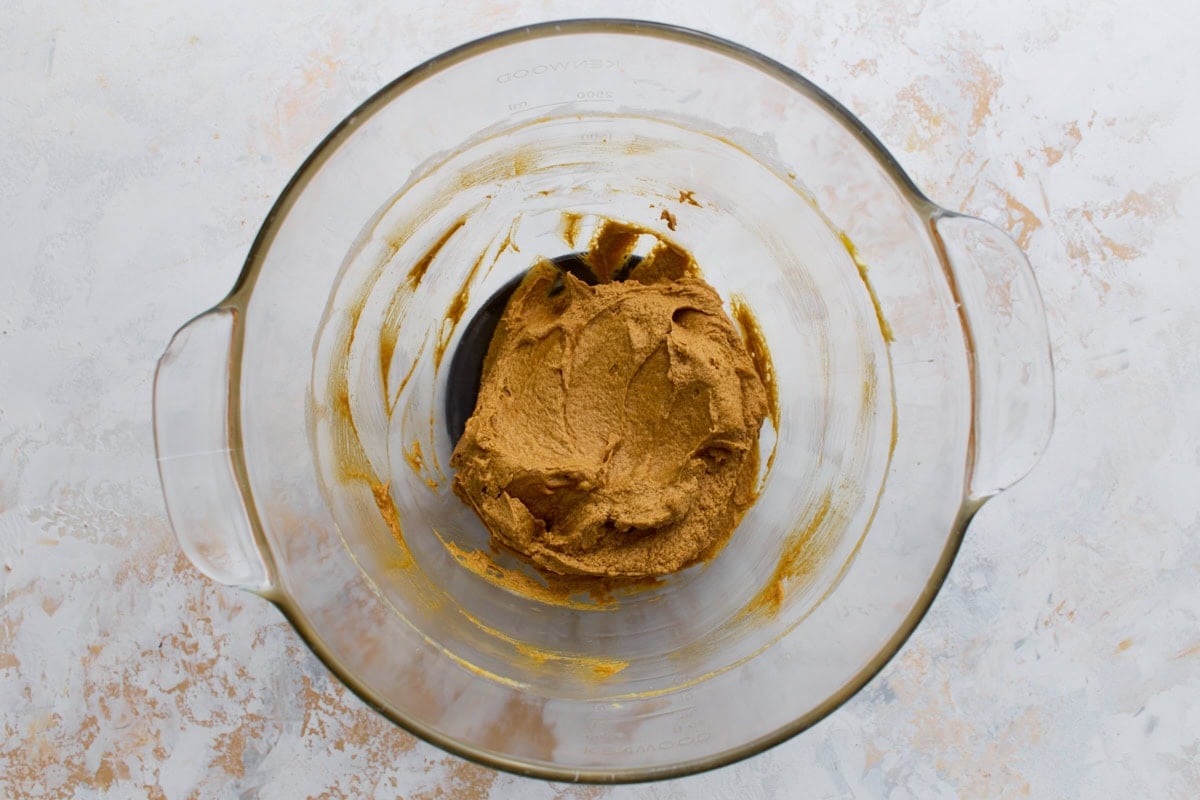 A glass mixing bowl with creamed butter, brown sugar, and molasses forming a fluffy golden base for the gingerbread dough.