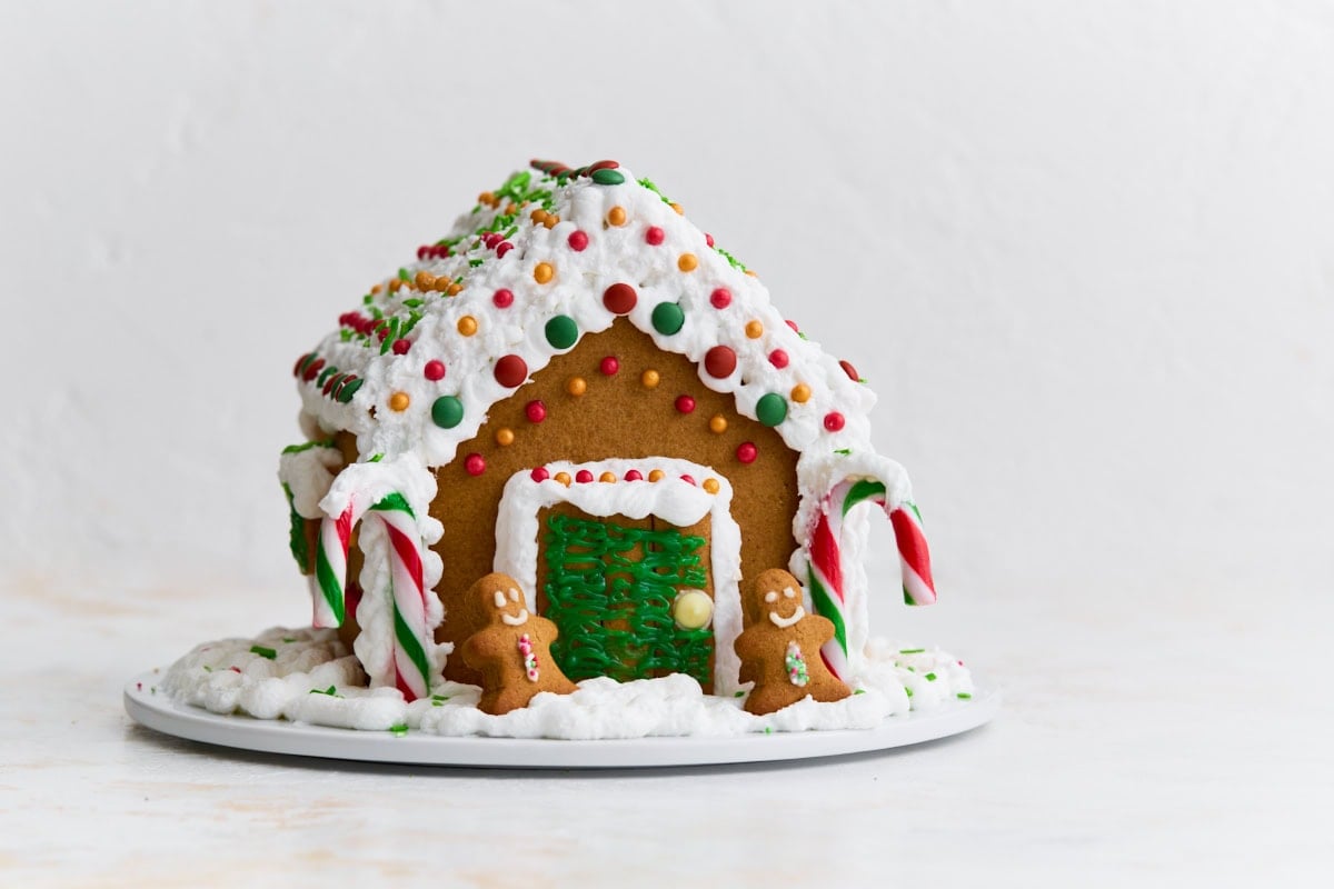 The completed gluten-free gingerbread house shown from the front, with candy canes framing the door and two small gingerbread people in front.