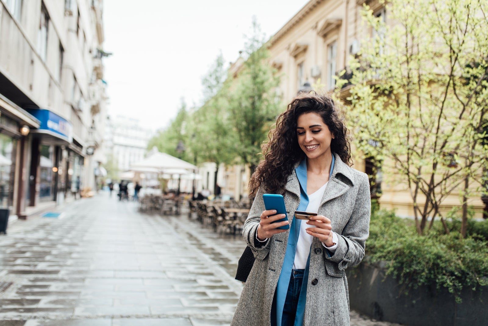A woman walking around a city with her phone and a credit card in her hands