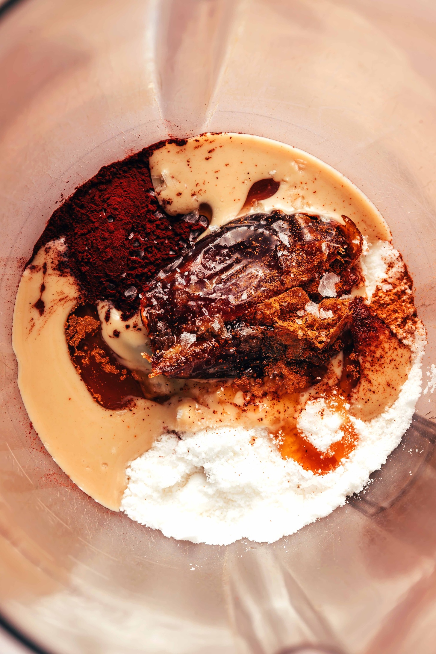 Blender with tahini, cocoa powder, medjool date, salt, cinnamon, collagen, coconut milk powder, and hot water
