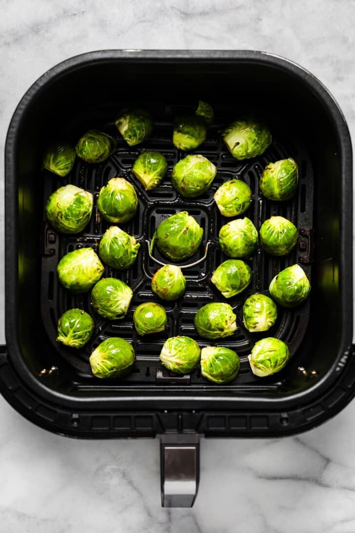 Seasoned Brussels sprouts in air fryer basket before cooking.