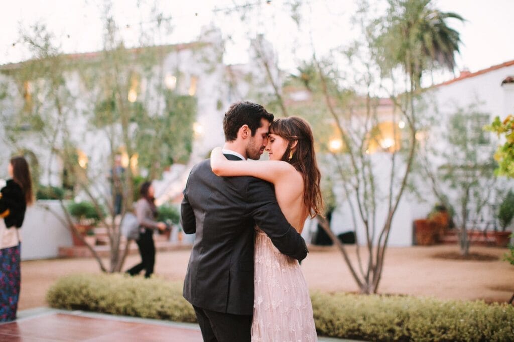 A bride and groom embrace in a courtyard outside of a Spanish-style home