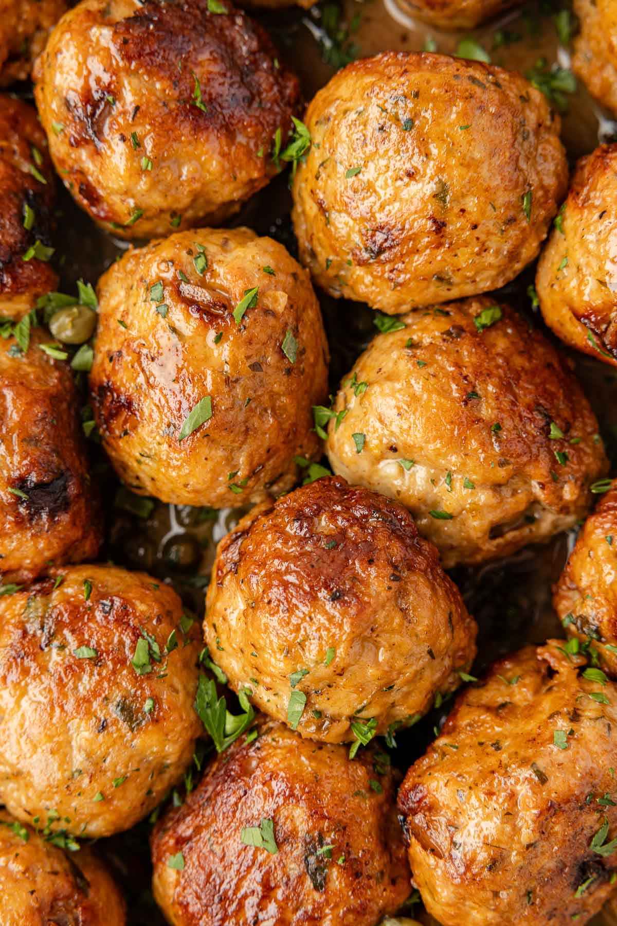 Close-up of several browned Chicken Piccata Meatballs garnished with chopped herbs.