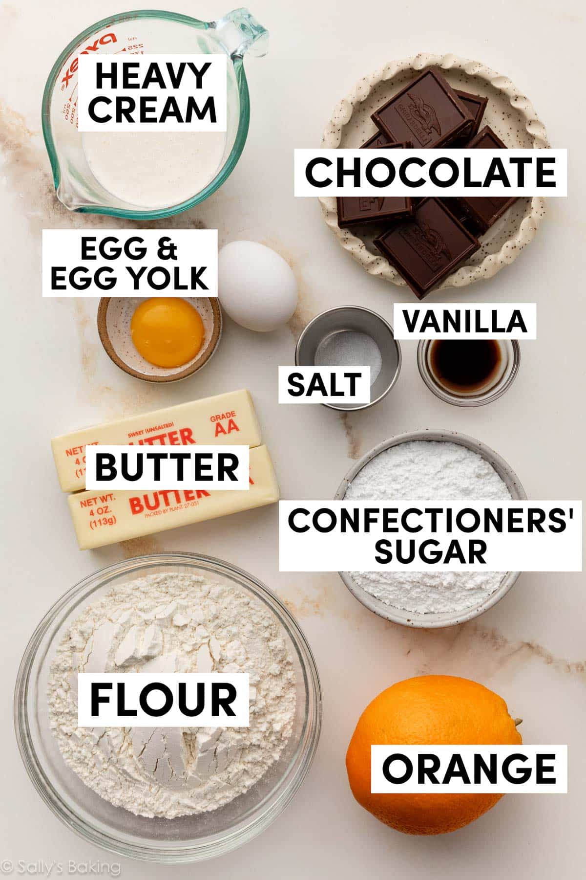 ingredients in bowls including flour, confectioners' sugar, orange, heavy cream, butter, and eggs.