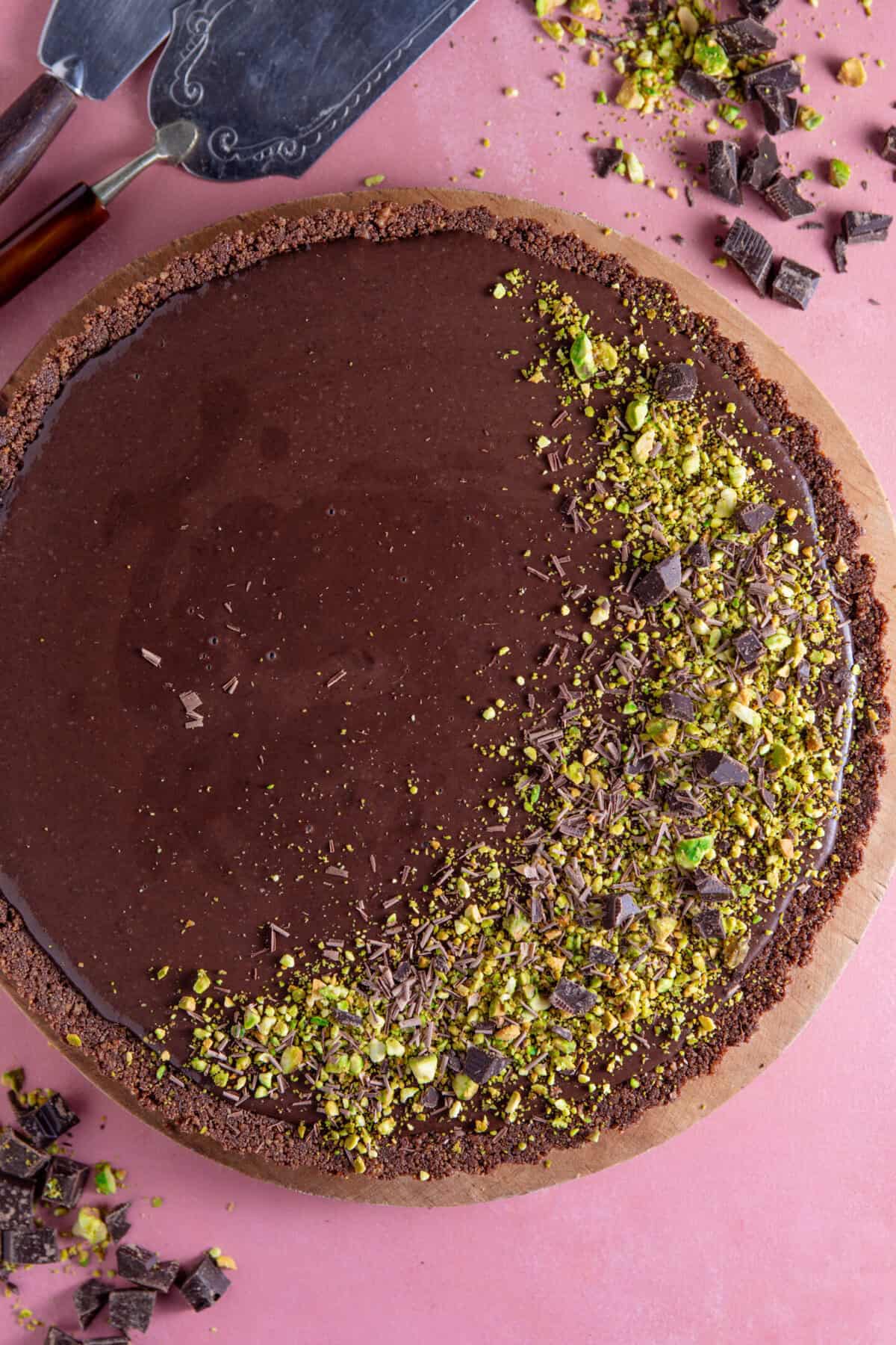 A process shot for a gluten free chocolate tart showing the finished chocolate tart decorated with crushed pistachios.