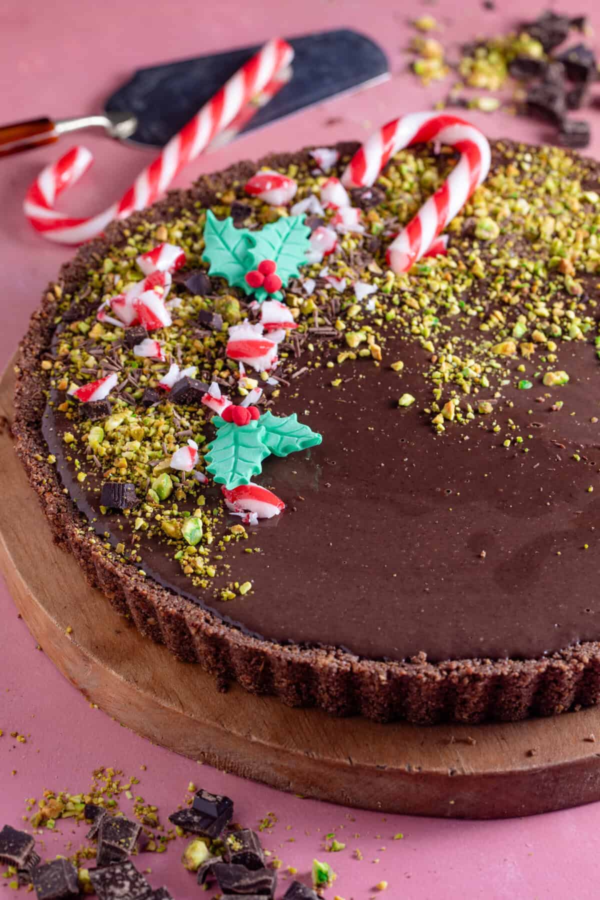 A no bake, gluten free chocolate tart decorated with crushed pistachios, candy canes and edible holly.