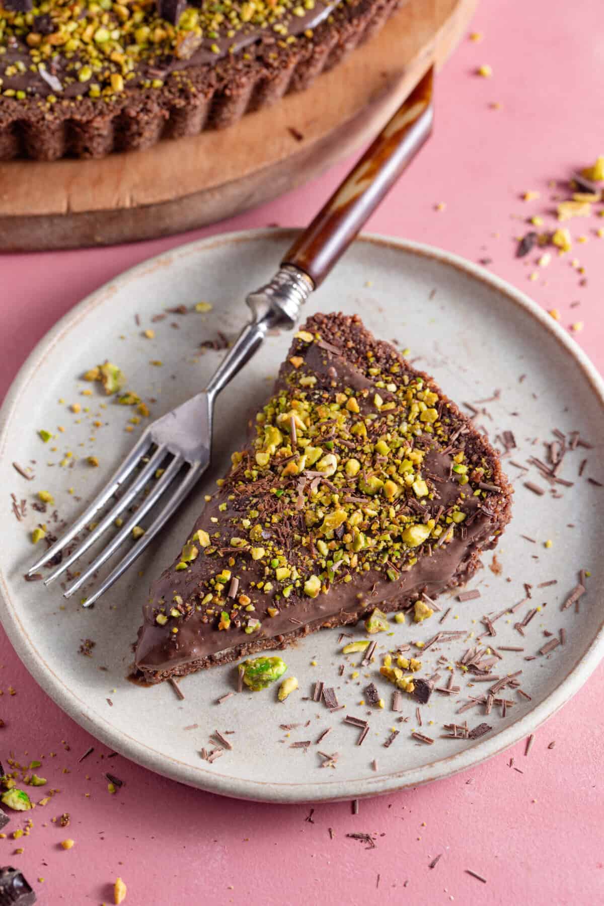 A slice of gluten free chocolate tart on a plate with crushed pistachio.