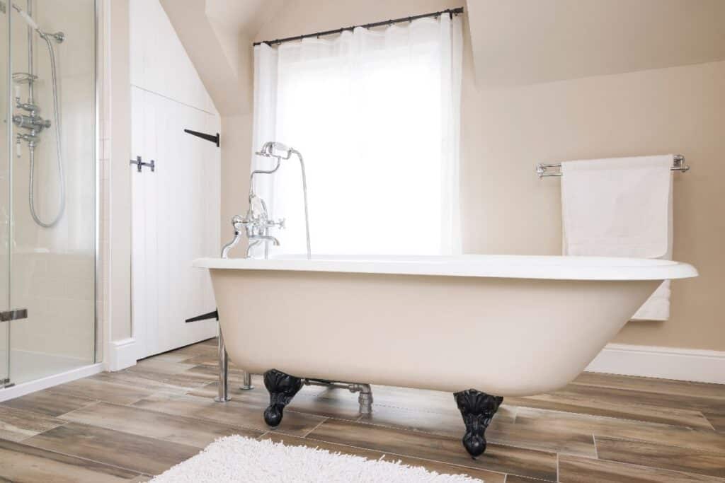 Elegant neutral bathroom with freestanding roll top bath, walk in shower and wooden floor, showing how an updated bathroom can increase home value.