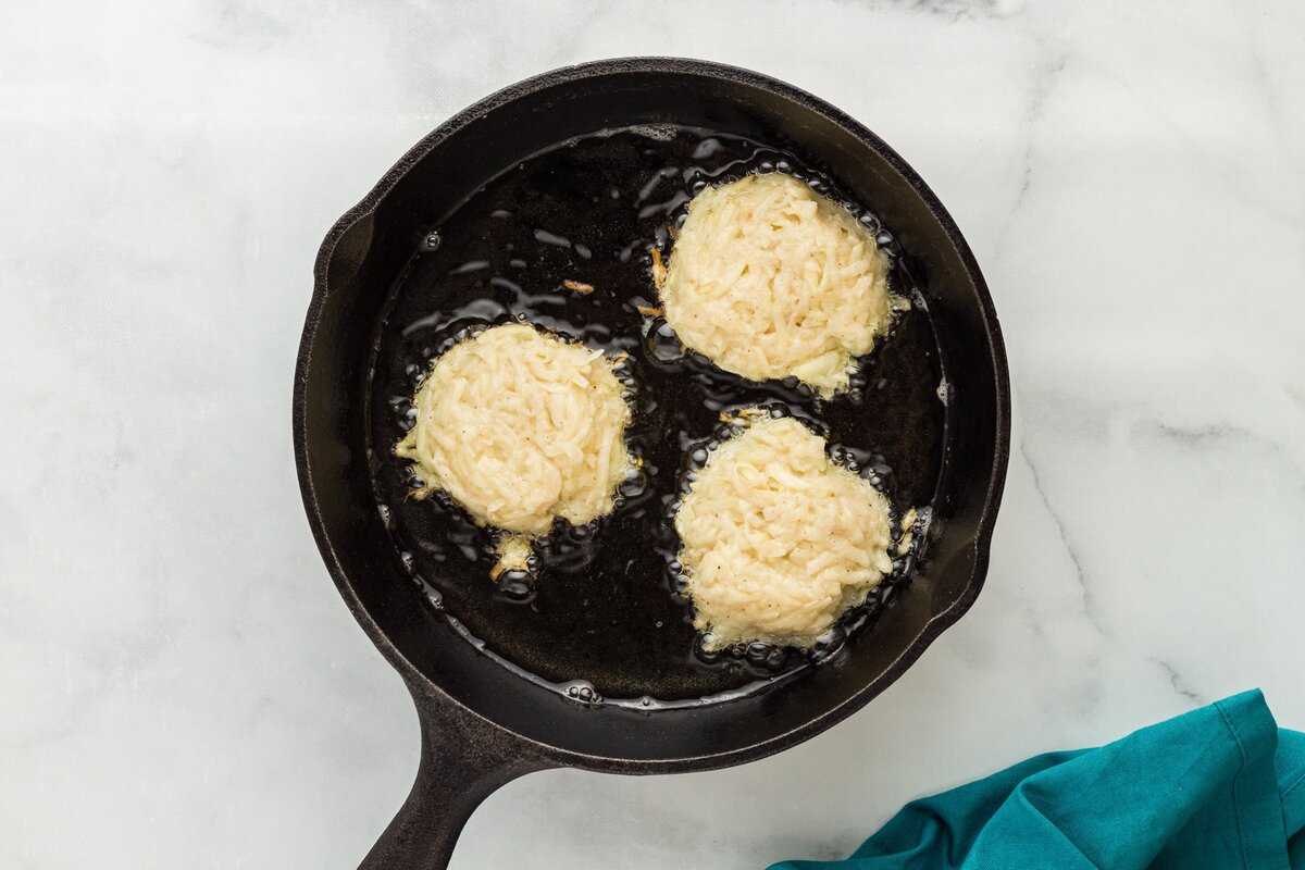 Latke patties frying in hot oil in a cast-iron skillet.