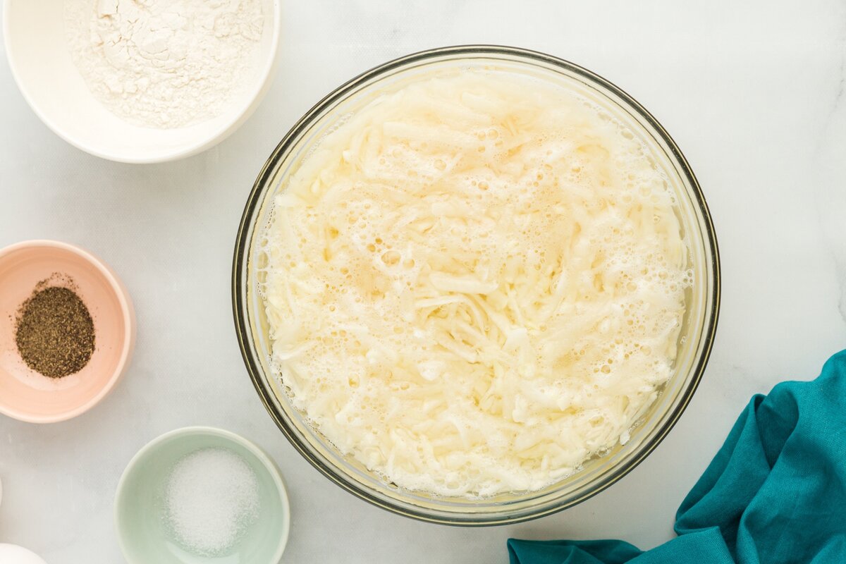 Grated potatoes soaking in cold water in a glass bowl to remove excess starch.