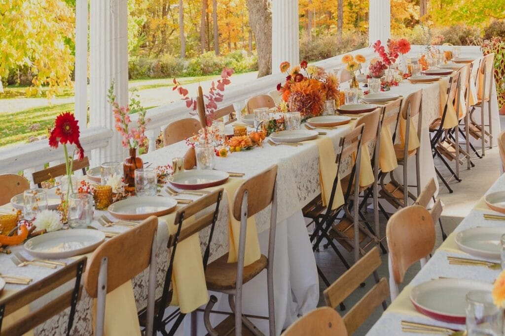 Long reception tables covered in lace tablecloths are decorated with a variety of floral arrangements on the verandah of a home