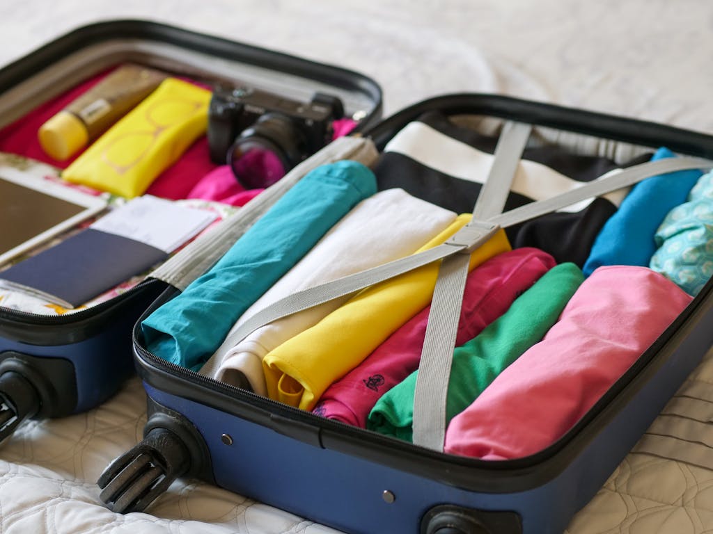 Open carry-on neatly packed with colorful clothes and travel essentials. Save money by not checking bags and travelling with just a carry-on