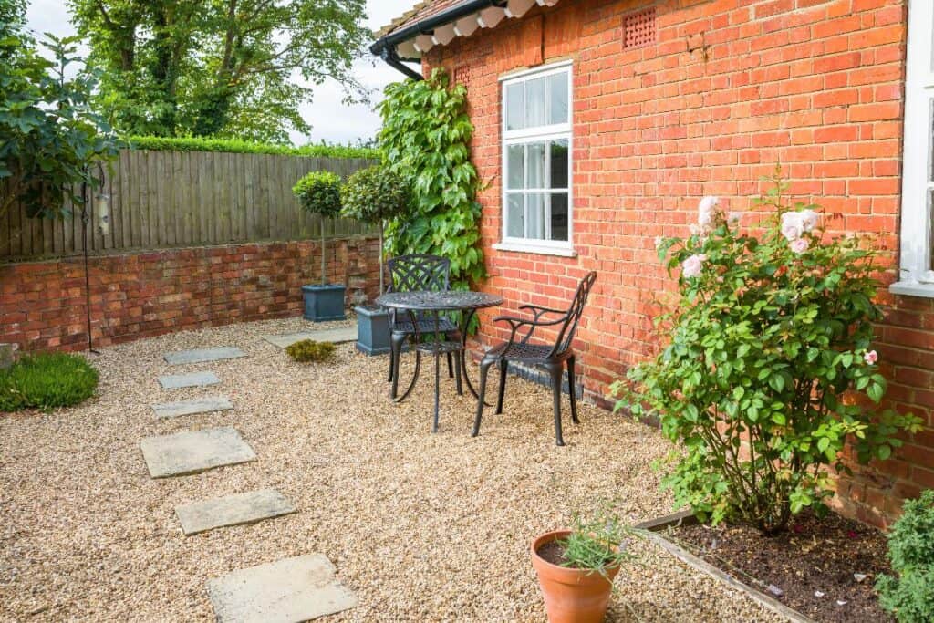 Neat gravel garden with bistro set, potted plants and brick wall, showing how simple outdoor landscaping can increase home value and kerb appeal.