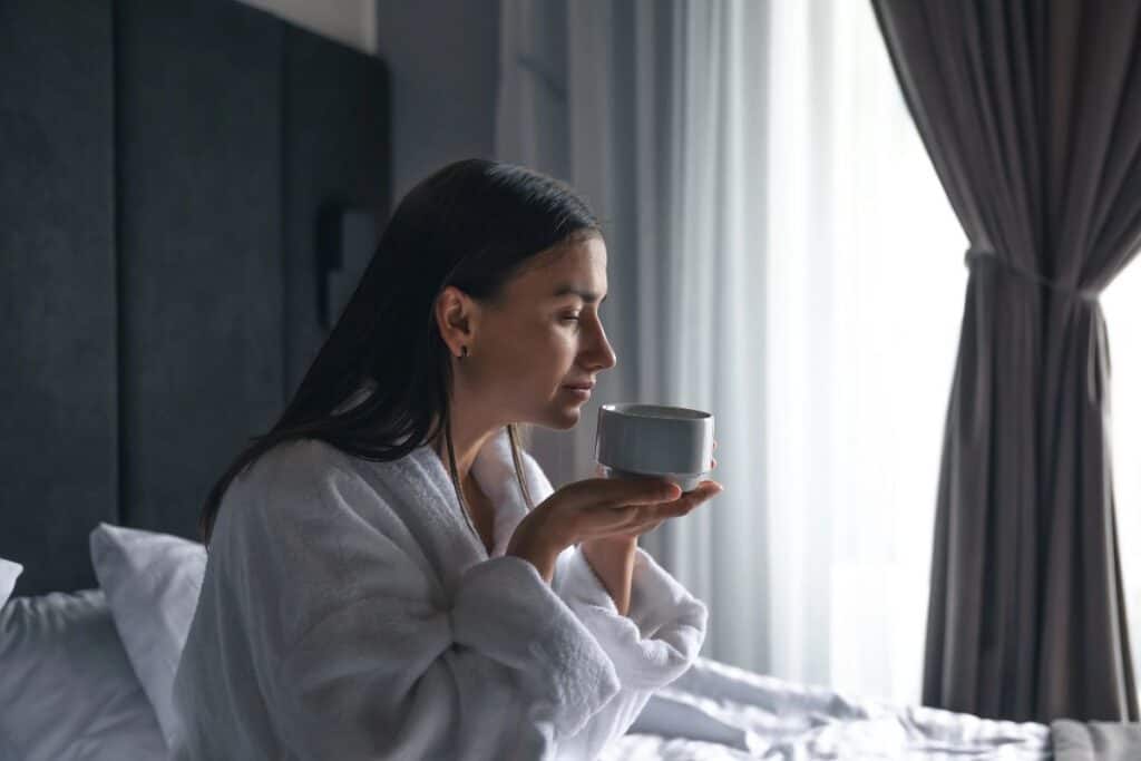 woman in a dressing gown having a hot drink by the window on a dark morning